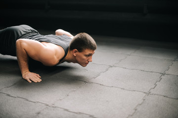 Fototapeta na wymiar Muscular young fit man with beautiful body doing push-ups exercise on the floor with black mats during sport workout training in modern dark gym. Concept of healthy lifestyle, physical sport activity.