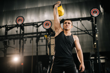 Young muscular man with perfect beautiful body wearing sportswear lifting heavy free weights overhead during sport workout training in modern dark gym. Concept of healthy lifestyle.
