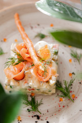 Traditional Russian salad Olivier. Salad is decorated with salmon and quail egg. Against the background of a wooden served table