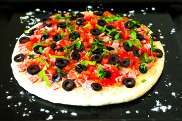Raw Pizza with salami and olives for cooking on dark background. Italian food background. Happiness is in small things. Close-up
