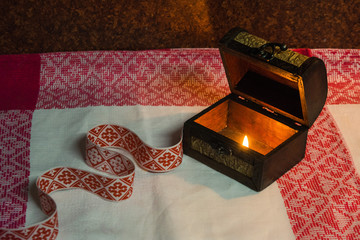 casket with a hot candle on a popular folk pattern tablecloths. next to it lies also a folk belt...