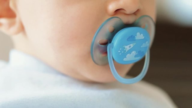 Close up of nice caucasian newborn baby on the bed and sucking a pacifier
