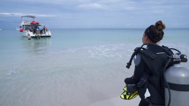 Slow Motion of young woman with aqualung walking towards boat, tourists at beach against sky - Montego Bay, Jamaica