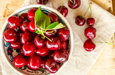 Beautiful bright red berries of sweet cherry. Close-up. Juicy sweet cherry berries in ceramic bowl on brown wooden table. Linen cloth. Vegetarianism, raw food concept. Fruit vitamin background.