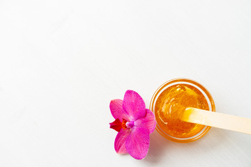 depilation and beauty concept - sugar paste or wax honey for hair removing with wooden waxing spatula sticks on flower background. copyspase.