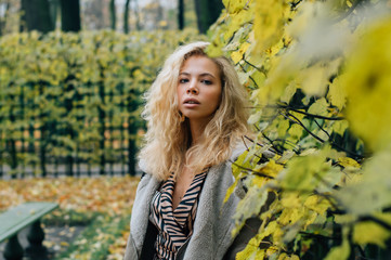 Young blond girl staying near trees  in public park