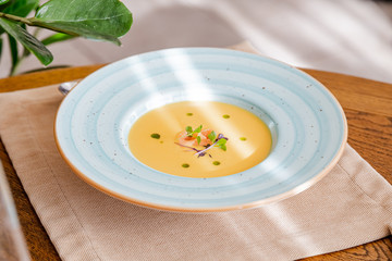 cream of salmon soup, in a bright blue plate, decorated with pieces of salmon, microgreens and butter. On the background of a wooden table.
