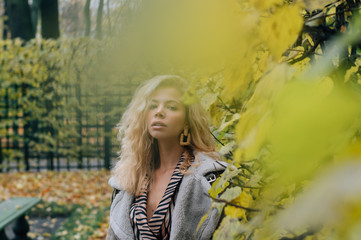 Young blond girl staying near trees  in public park