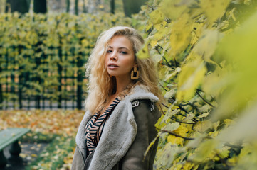Fototapeta na wymiar Young blond girl staying near trees in public park
