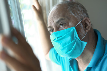 senior man with face mask looking through window 