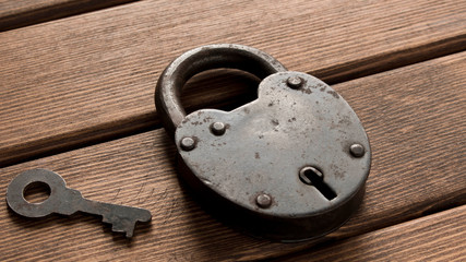 Old padlock with key on wooden background. Security concept.
