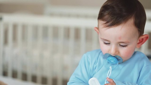 Close up of nice caucasian newborn baby on the bed and sucking a pacifier