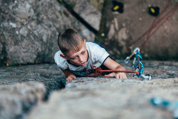 A child climber in a white T-shirt, climbs a steep rock.