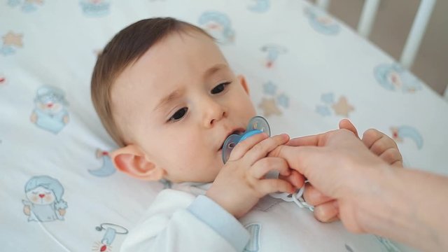 Close up of nice caucasian newborn baby on the bed and sucking a pacifier