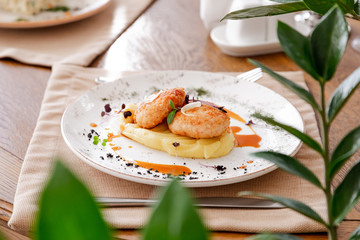 mashed potatoes with cutlet, on a beautiful white plate. The dish is decorated with micro-greens. Against the background of a wooden table in the interior.