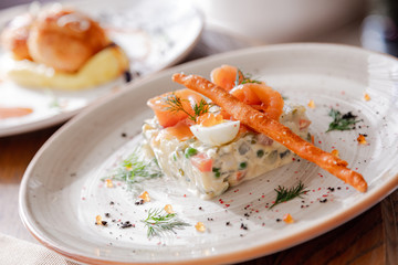 Traditional Russian salad Olivier. Salad is decorated with salmon and quail egg. Against the background of a wooden served table