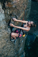 Young strong girl rock climber in a bright T-shirt climbing on a rock.