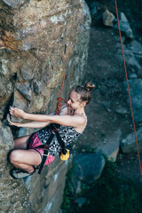 Young strong girl rock climber in a bright T-shirt climbing on a rock.