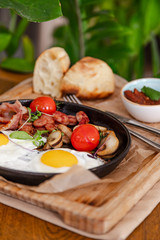 English breakfast. Fried eggs with fried sausages, bacon, tomatoes and mushrooms. On a wooden with bean paste.