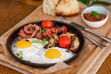 English breakfast. Fried eggs with fried sausages, bacon, tomatoes and mushrooms. On a wooden with bean paste.