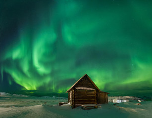 Landscape with northern lights over a wooden house on the coast of the Barents Sea on the Kola...