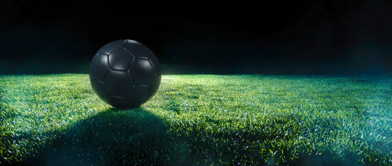 Black Football on an illuminated empty sports field at night.