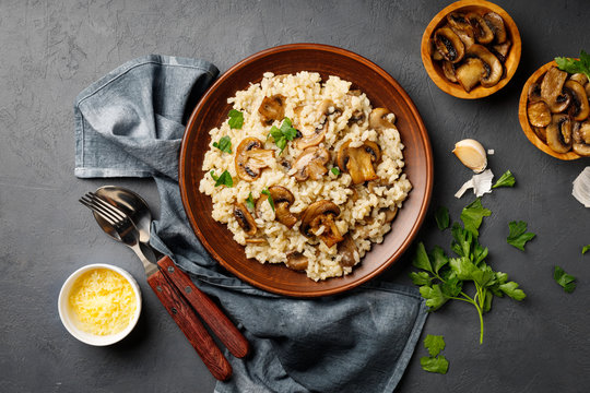 A dish of Italian cuisine - risotto from rice and mushrooms in a brown plate on a black slate background. Top view. Flat lay.