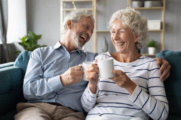 Overjoyed mature family couple sitting on couch, enjoying pleasant conversation, laughing at jokes...