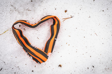 St. George ribbon in the form of heart on white snow in the forest in the spring afternoon.