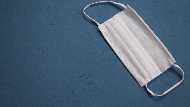 a doctor wearing blue sterile gloves is putting a white surgical mask on a blue floor. Coronavirus 2019-nCoV. Covid-19, isolated background