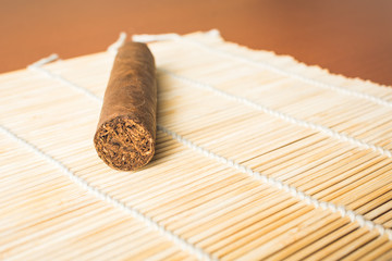 Expensive cigar on white bamboo mat lying on table.