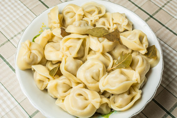 Handmade boiled meat dumplings with bay leaves in large plate on kitchen table.