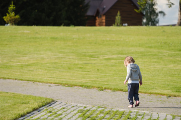 Fototapeta premium Small child walks along an alley in green field.