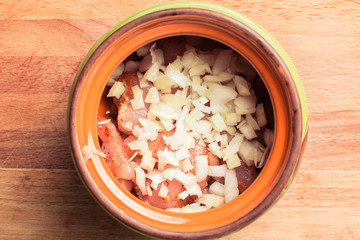 Raw sliced chicken breast fillet sprinkled with onions in ceramic pot for cooking in oven.