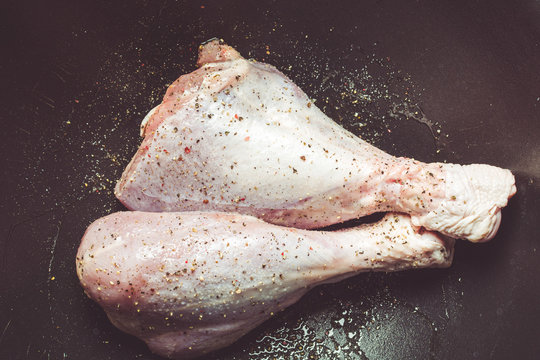 Delicate raw turkey legs sprinkled with salt and pepper in large cauldron for roasting in oven.