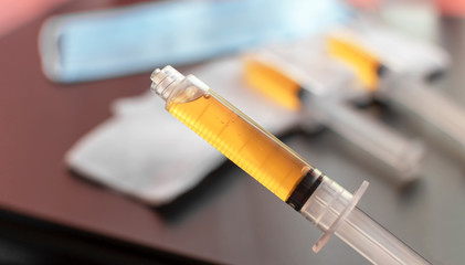 Blood plasma in a syringe on a blurred background. Blood plasma as a solution for the treatment of coronavirus. Platelet-rich plasma preparation for plasmolifting therapy. Selective focus. - obrazy, fototapety, plakaty