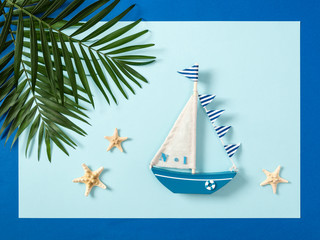 Fototapeta na wymiar Nautical composition with sailing boat, palm tree leaves and sea stars on blue background, flat lay