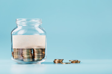 A glass jar with coins and a sticker with free space for text, on a blue background.