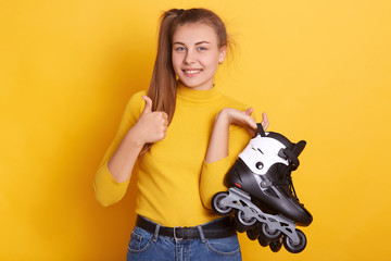 Horizontal shot of positive female with ponytail, wearing yellow shirt and jeans, holding rolling...