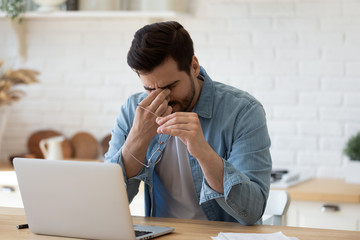 Tired young man work on laptop take off glasses massage eyes suffer from blurred vision or...