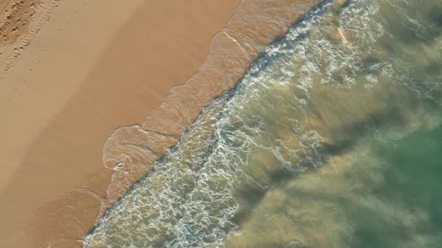 Drone Zoom Out View Of Calm Waves Slowly Rolling On Beach. Aerial Drone Up Shot Of Ocean Waves And Sandy Beach, Natural Calm Texture Of Sea Foam Against Yellow Sand Beach Shot From Above