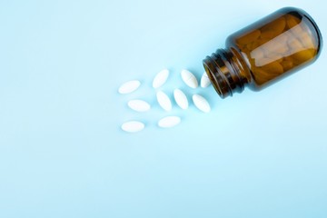 Pills tablets spilling out of drug bottle and isolated on blue background.Top view with copy space.Medicine concept.health care and medical.Medications against the COVID-19 and other condition disease