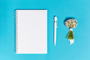 Notebook with blank paper, pen and bunch of daisy flowers on blue background, top view