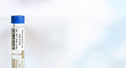 Coronavirus Covid-19 vaccine concept - small glass vial with blue cap on white table, closeup banner space for text right side (sticker is own design with dummy data and barcode, not a real product)