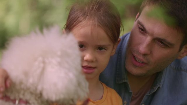 Beautiful happy family is having fun with bichon dog outdoors in the park