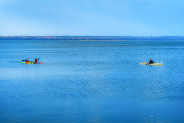 A company of young people on kayaks is training at sea. Four multi-colored canoes sail in the blue sea. Spring Canoeing in the Lake