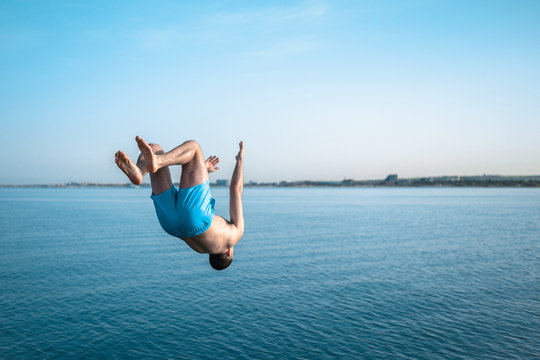 The young guy makes a jump back to the sea. The man does a backflip into the water. The guy jumps in the beautiful blue sea - Powered by Adobe