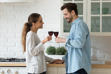 Happy millennial couple tenants clink glasses cheers feel excited moving into new home together, smiling young husband and wife celebrate relocation to own house, enjoy romantic date in kitchen