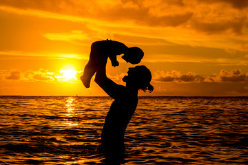 Father throws up a little son against the backdrop of the ocean and an incredible sunset