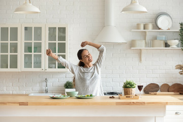 Happy millennial girl preparing healthy breakfast having fun in bright modern kitchen at home, overjoyed young woman cooking in new house or apartment feel excited moving relocating to own dwelling